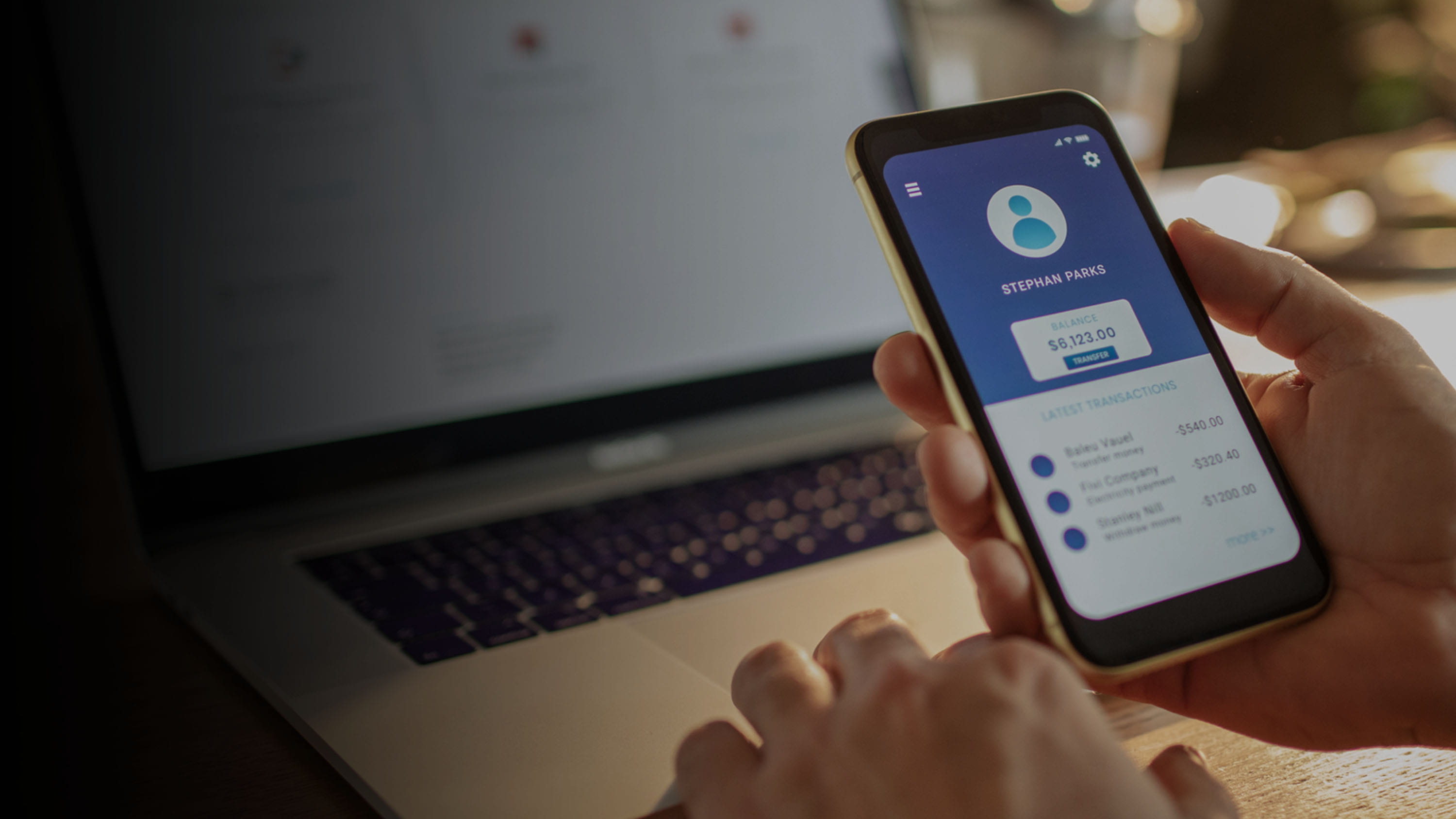 Person using a bank mobile app on their cell phone and their laptop in front of them.